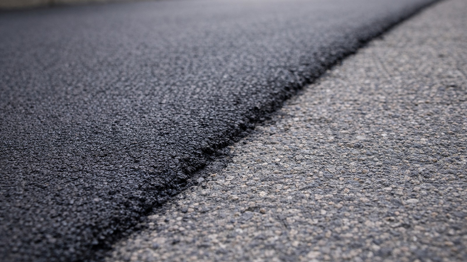 Close-up of a clean asphalt repair seam where new pavement blends into older pavement