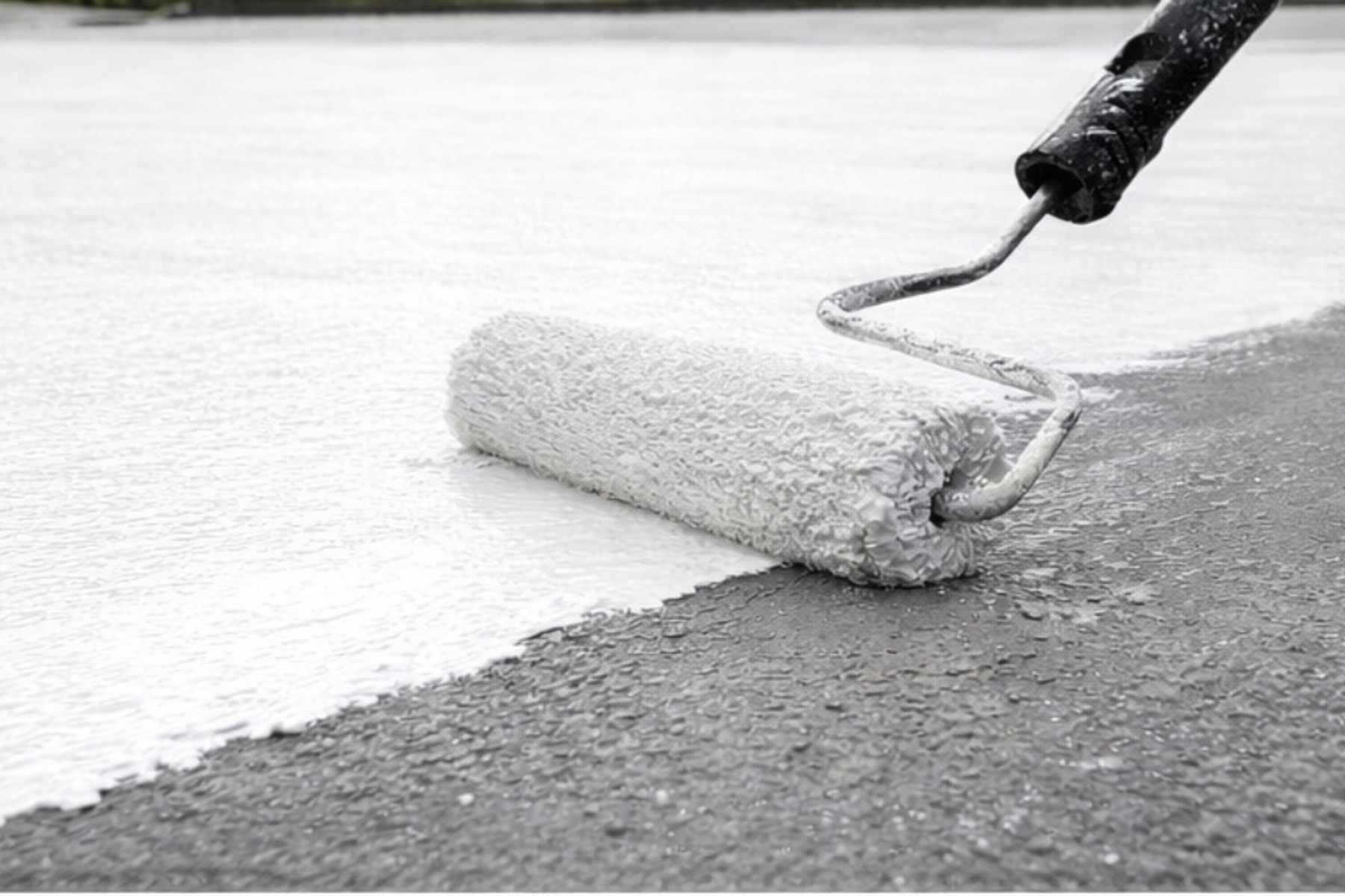 Close-up of a roller applying a reflective roof coating across a flat surface with a clean wet edge